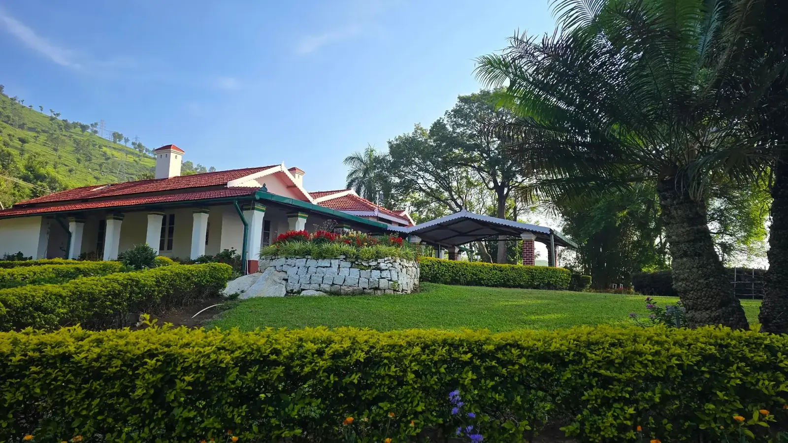 A heritage bungalow in the Nilgiris with red-tiled roof, clipped hedges and a tea-covered hillside behind